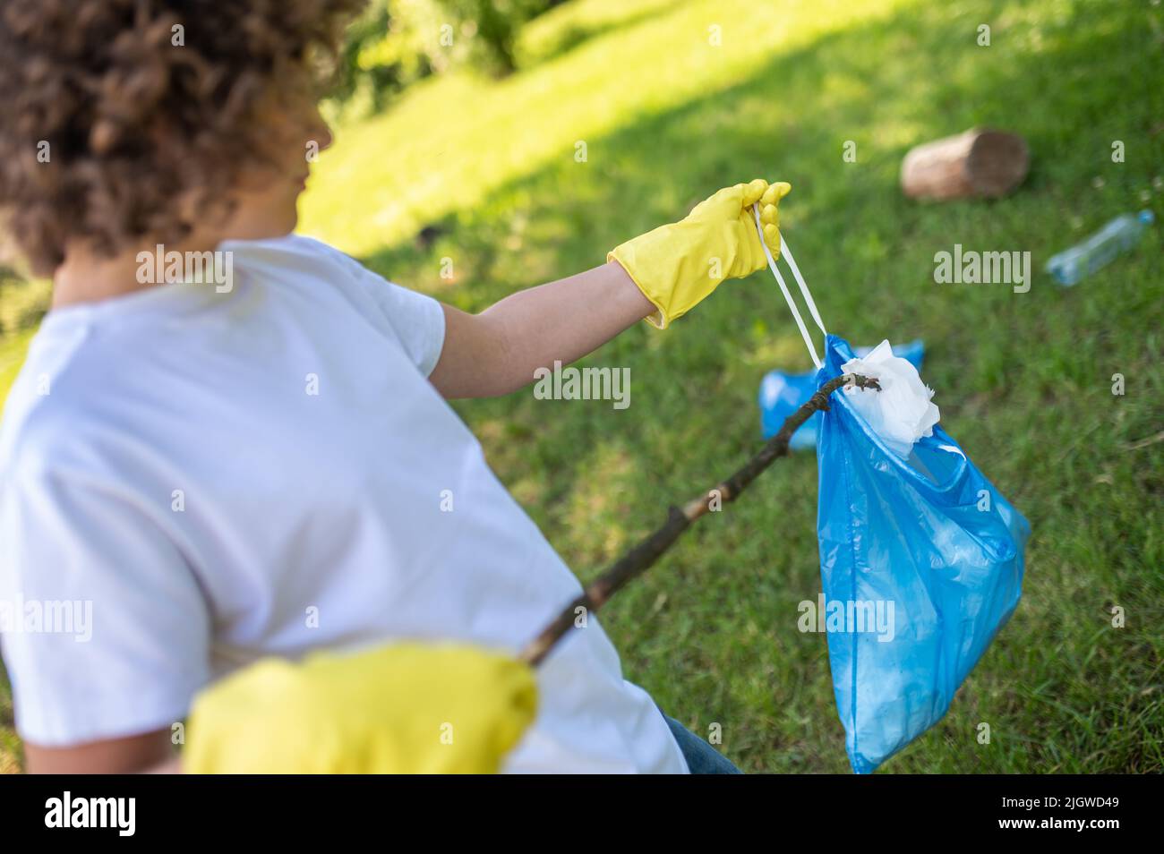 Teen tenendo un bastone e gehering la lettiera sull'erba Foto Stock