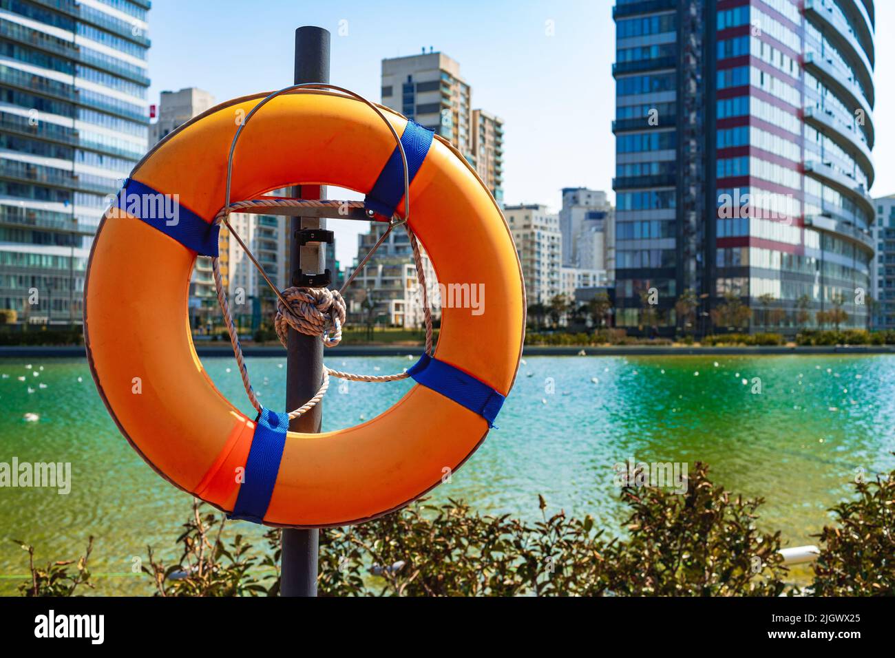 Salvagente arancione appeso su un pilastro vicino all'acqua nel complesso residenziale Foto Stock