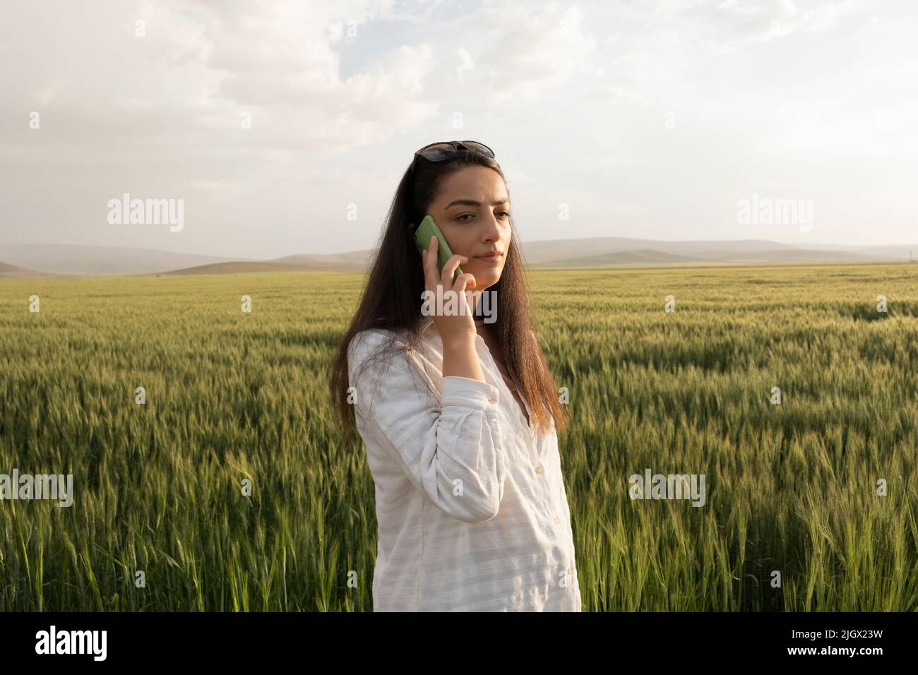 Agricoltore femminile, giovane agricoltore femminile in piedi vicino al suo campo di grano e parlando al telefono. Donna di affari moderna caucasica che lavora in fattoria. Foto Stock