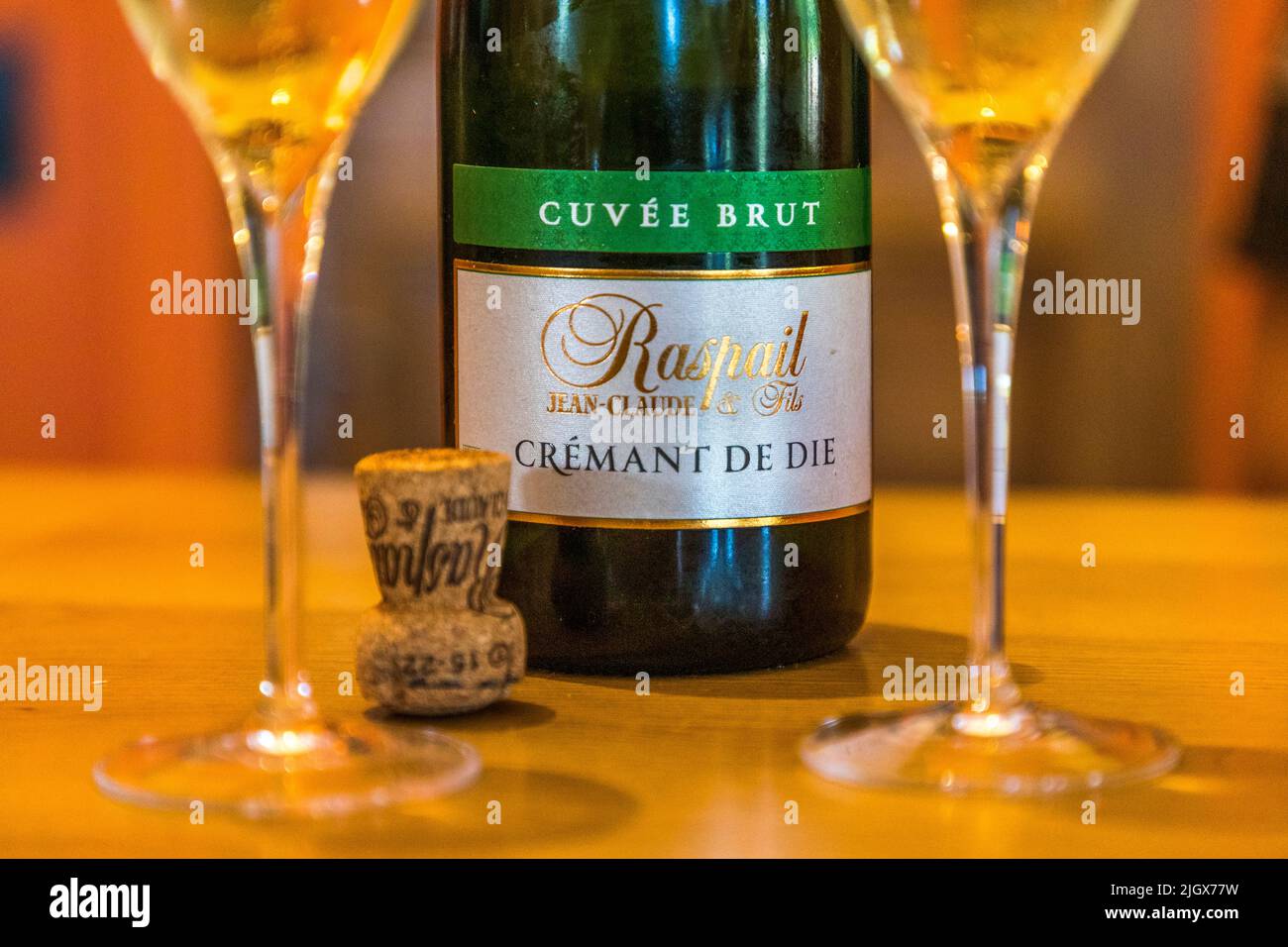 Una bottiglia di "Raspail Jean-Claude & Fils, Cuvée Brut, Crémant de Die" è posata con il suo tappo e due bicchieri pieni su un tavolo di legno – una degustazione nell'azienda vinicola di Saillans, Drôme, Francia. L'azienda vinicola è stata fondata nel 1942 da Henriette e Marius Raspail. È gestita biologicamente dal 1997 da Frédéric Raspail, che produce il vino spumante da uve Clairette utilizzando il metodo tradizionale di fermentazione in bottiglia (méthode traditionnelle). Foto Stock