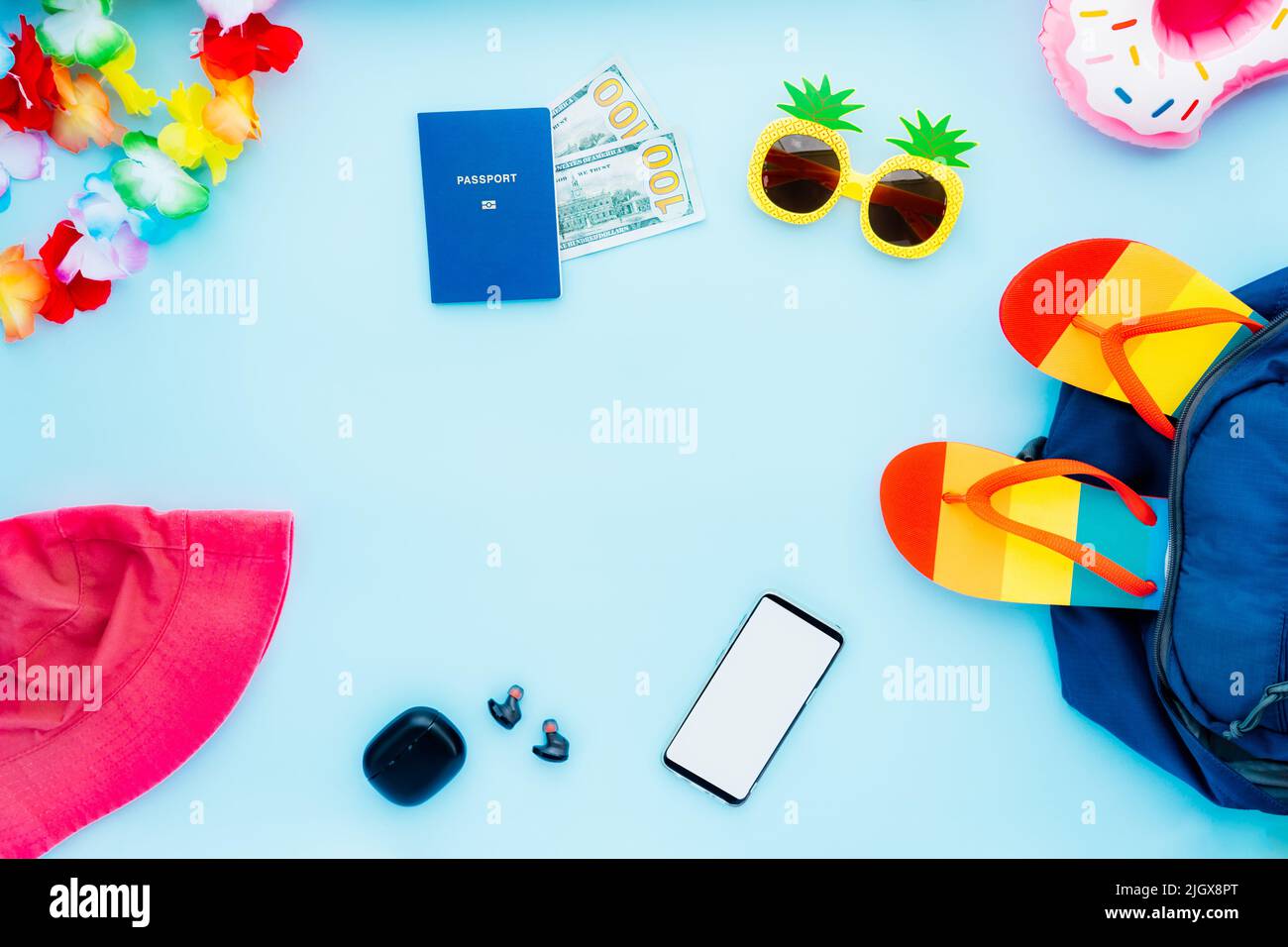 Vista dall'alto concetto di vacanza estiva con tutte le cose di viaggio necessarie. Zaino, cappello da secchio, occhiali da sole divertenti, infradito, passaporto biometrico, contanti, telefono Foto Stock