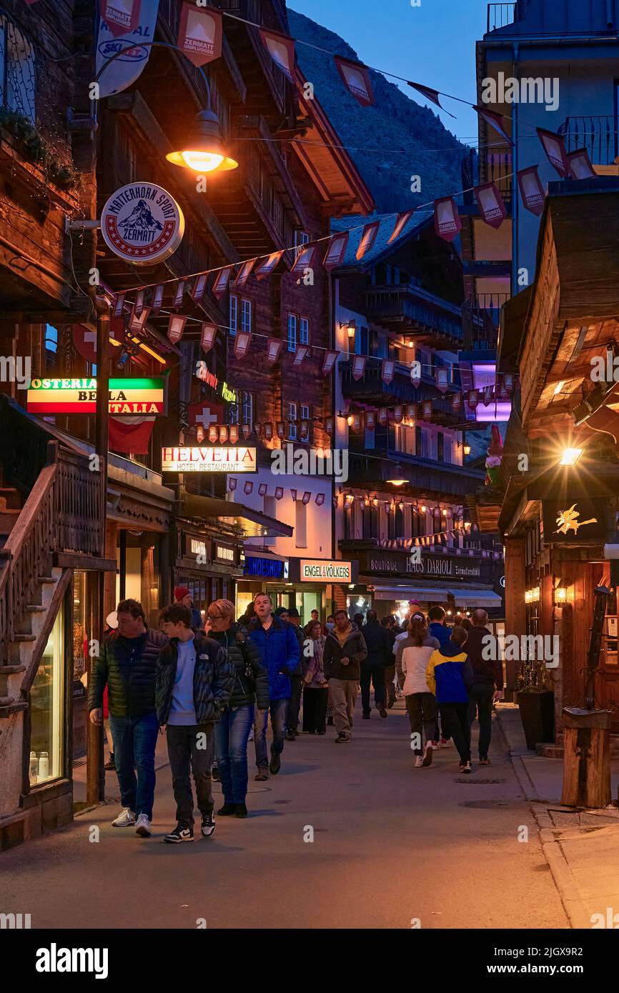 ZERMATT, SVIZZERA - Apr 11, 2022: Turisti che camminano e visitano una strada nella città di Zermatt al tramonto. Foto Stock