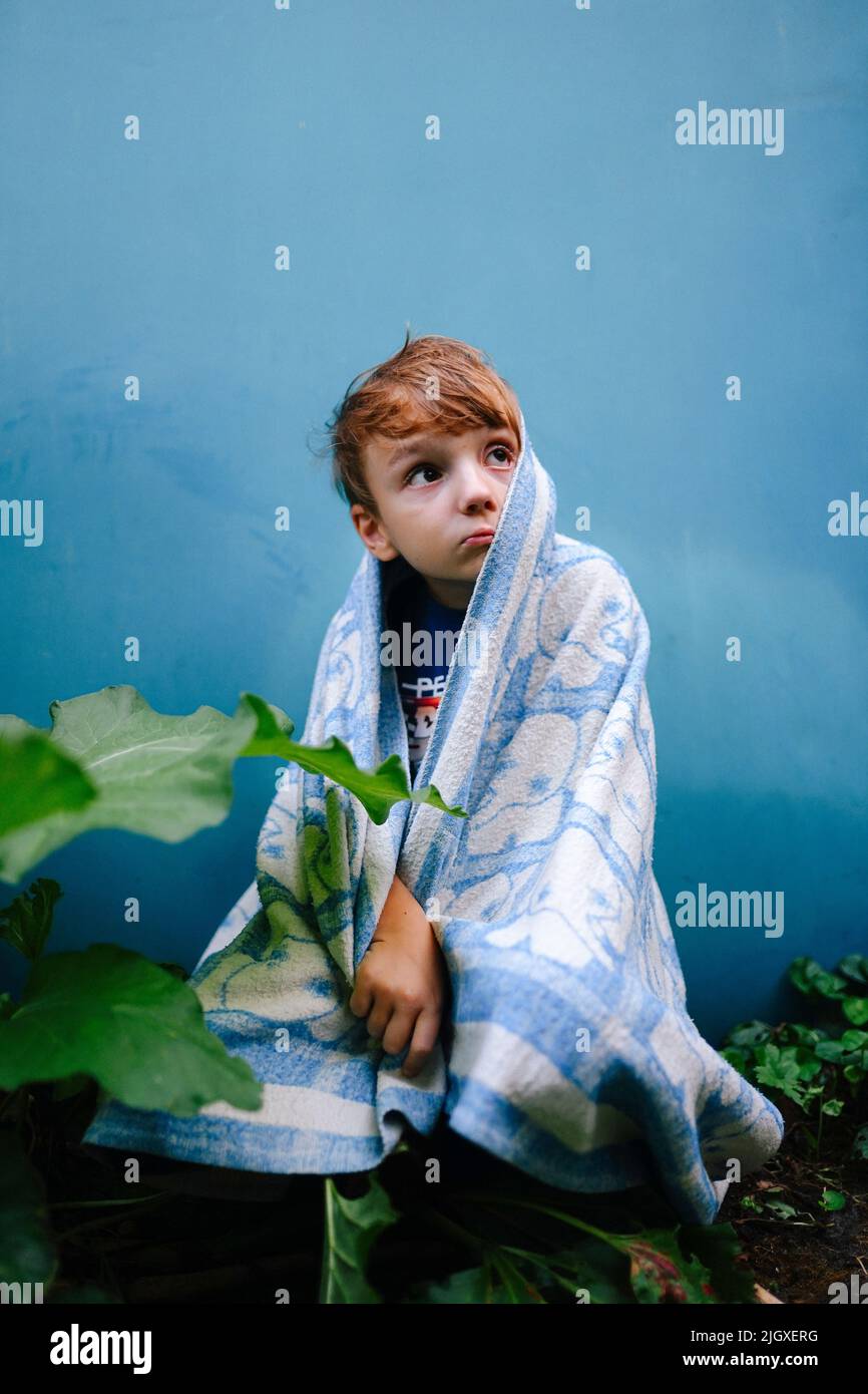 il bambino infelice si coprì con una coperta nel cortile Foto Stock