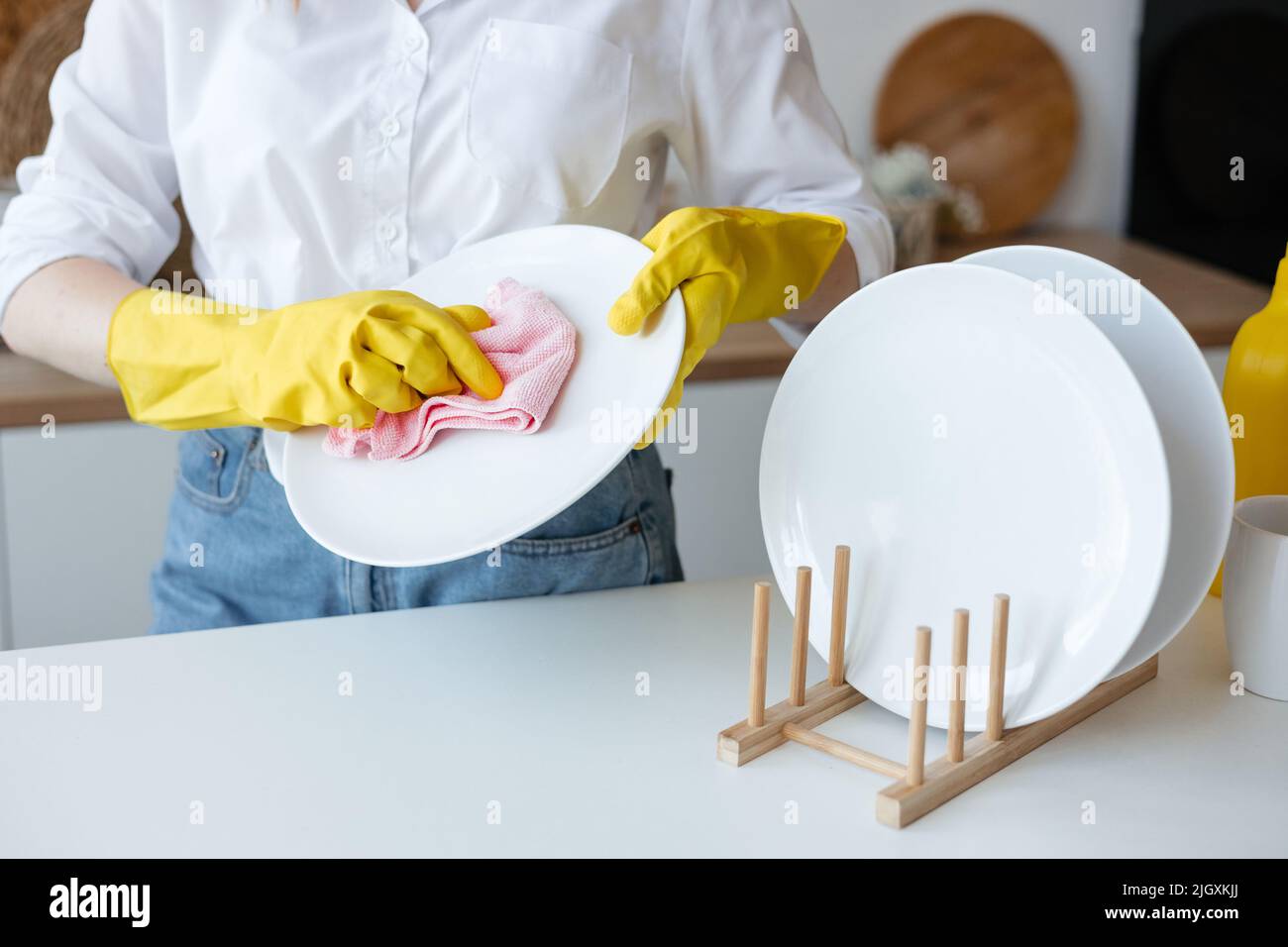 Ragazza strofinare un piatto pulito con uno straccio giallo in cucina Foto Stock
