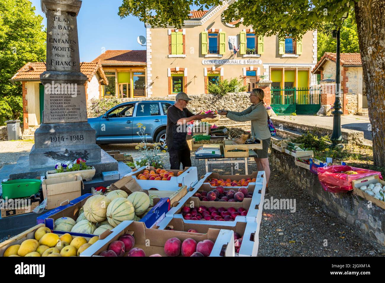La scrittrice di cucina Angela Berg acquista fiori e frutta al mercato settimanale nel villaggio di Plan-de-Baix, nella Drôme, in Francia, che conta 162 abitanti. Lo stand si trova proprio accanto al monumento funebre del villaggio, la cui iscrizione commemora i residenti morti tra il 1914 e il 1918. L'ex edificio della scuola e del municipio si trova sullo sfondo. Foto Stock