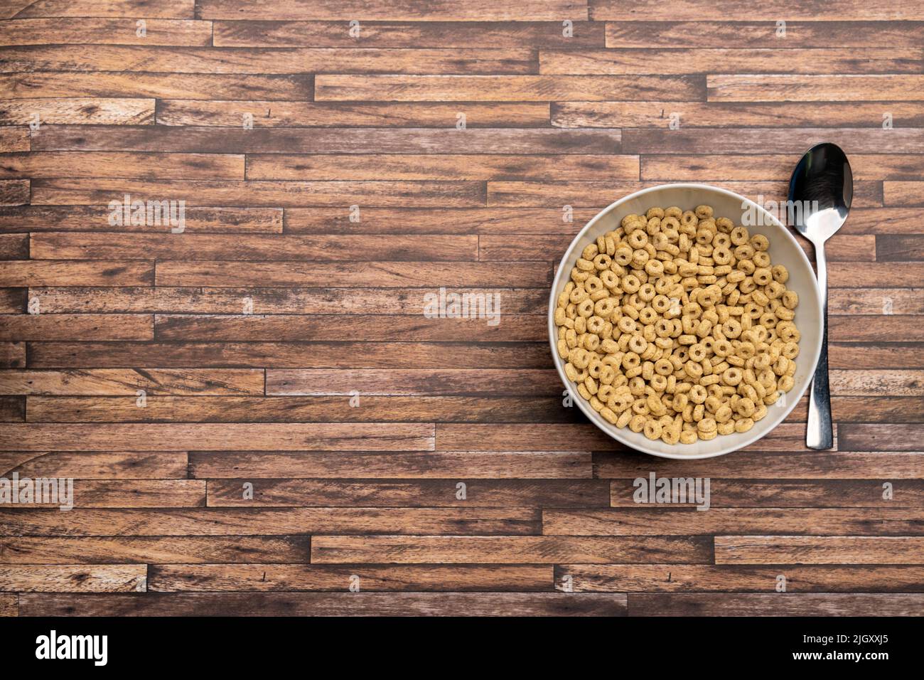 Cereali in un recipiente bianco con un cucchiaio su un tavolo di legno. Cornflakes rotondi per colazione. Guardando dall'alto verso il basso. I deliziosi anelli di grano sono uno spuntino. Foto Stock