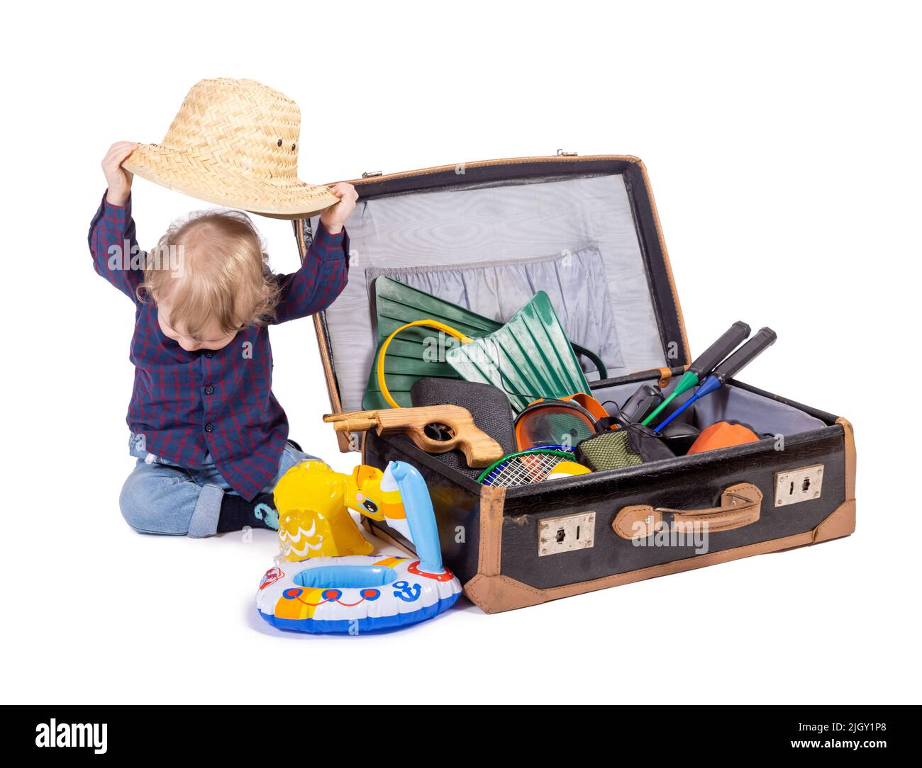 Un ragazzino siede accanto ad una valigia con attrezzatura da viaggio, su sfondo bianco Foto Stock