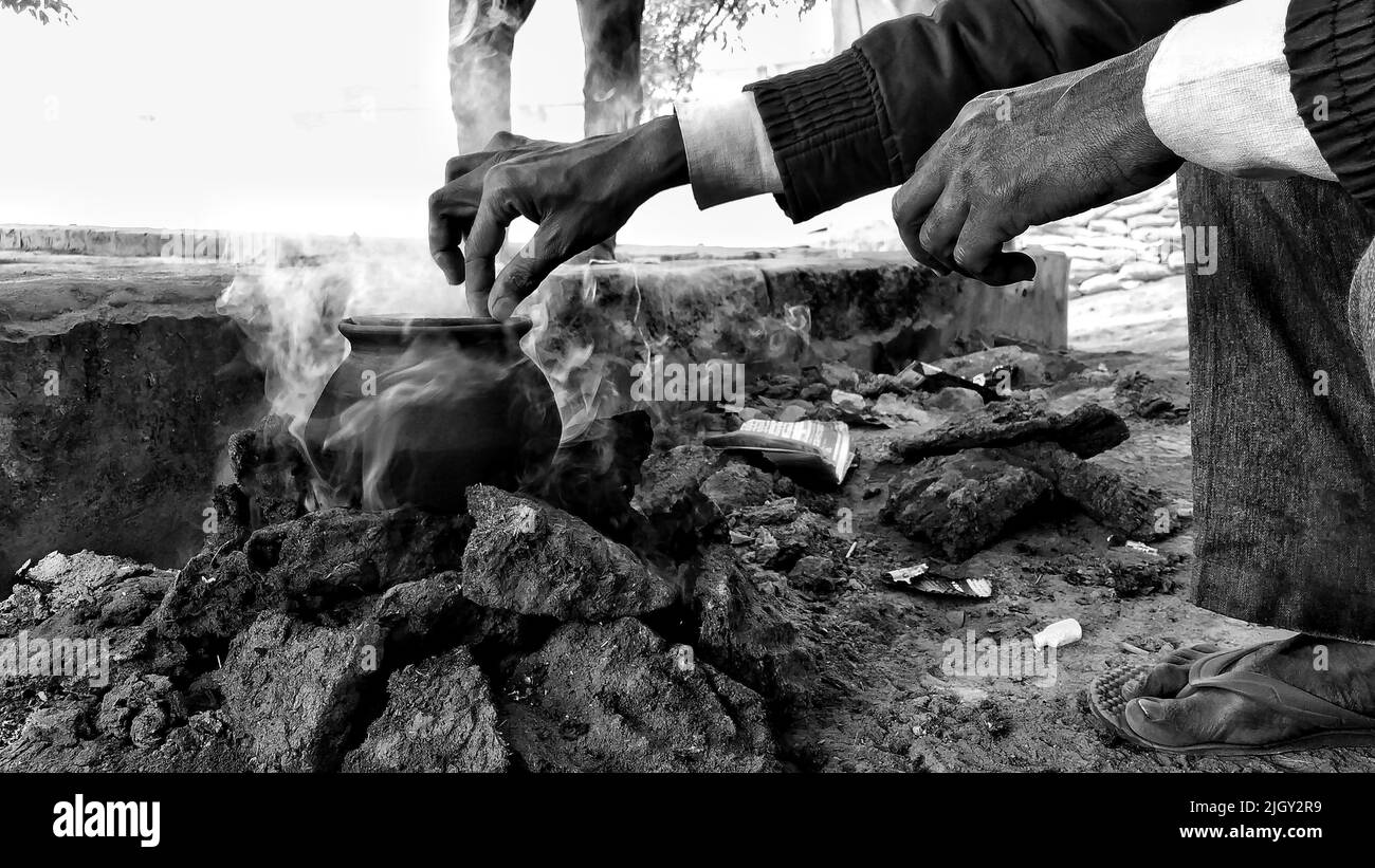 Un uomo sta cucinando il riso in una pentola di terra e il fumo sta alzando da esso, questo metodo di cottura è abbastanza comune nelle parti rurali dell'India. Foto Stock