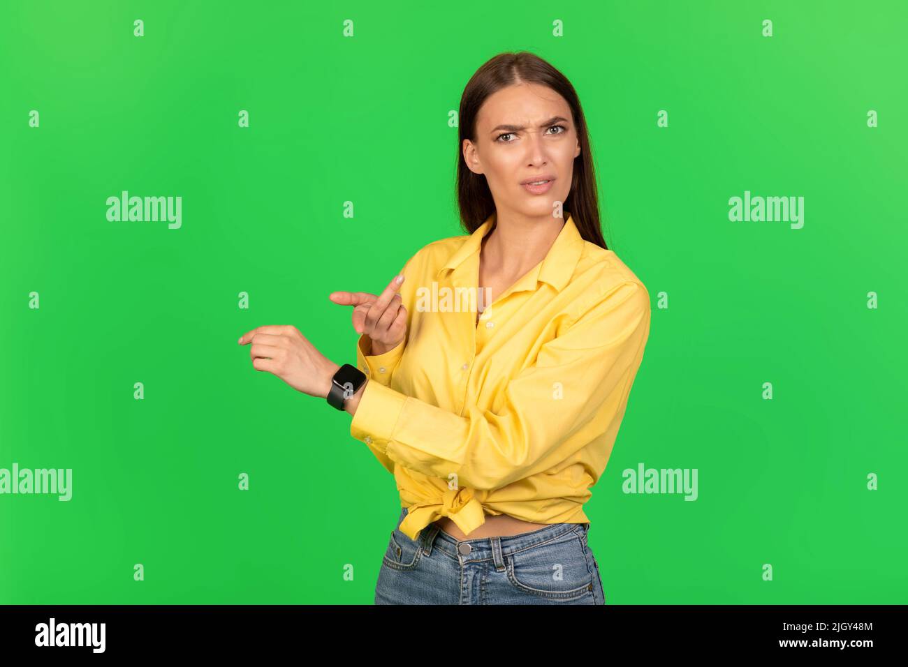 Spoeed Female Pointing Finger at Smartwatch over Green Studio background Foto Stock