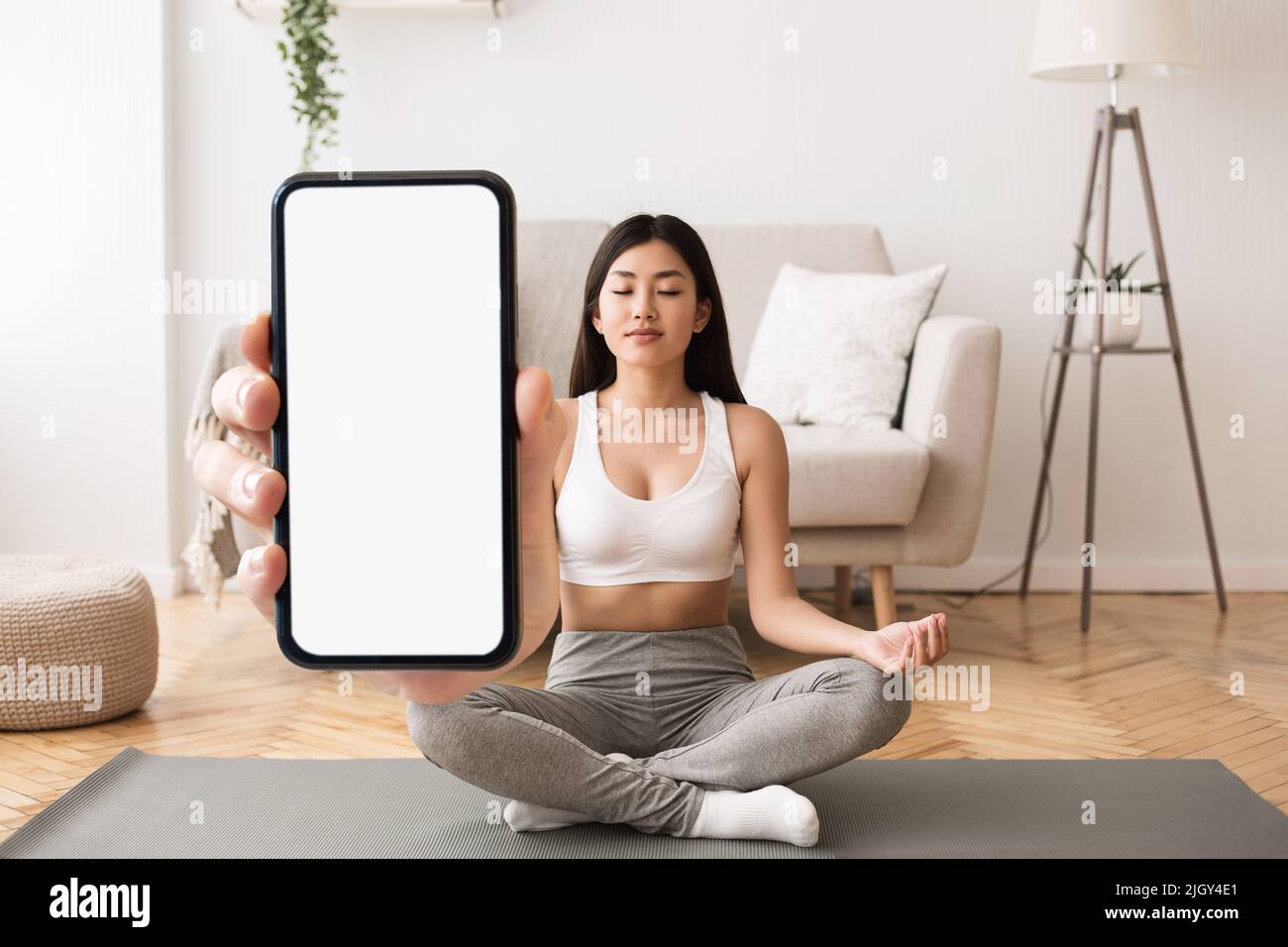 App Yoga. Calma giovane donna asiatica meditating e tenendo grande smartphone vuoto Foto Stock