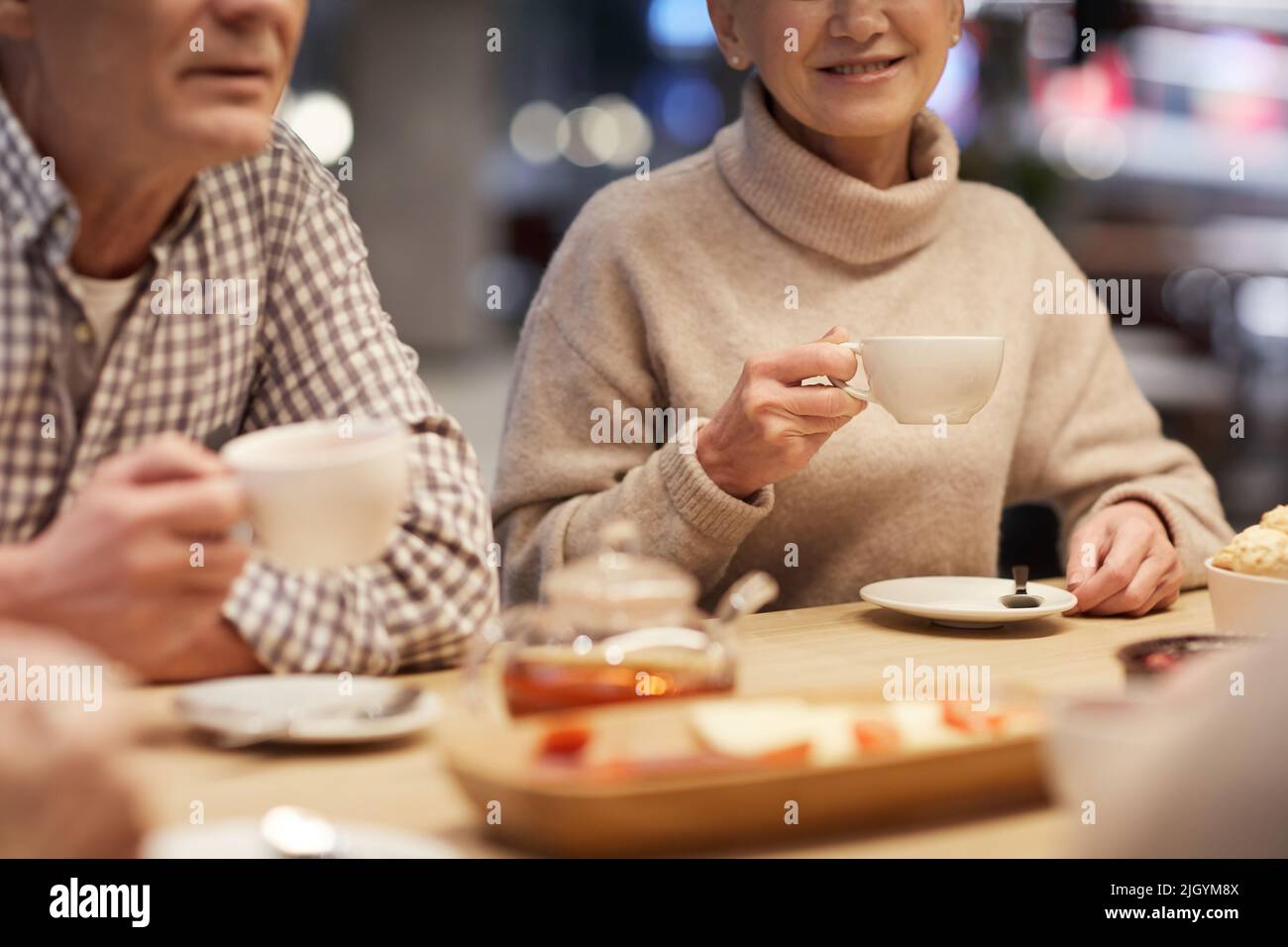 Primo piano di anziani positivi in abbigliamento casual seduti al tavolo e bere il tè mentre si discute le ultime notizie in caffè Foto Stock