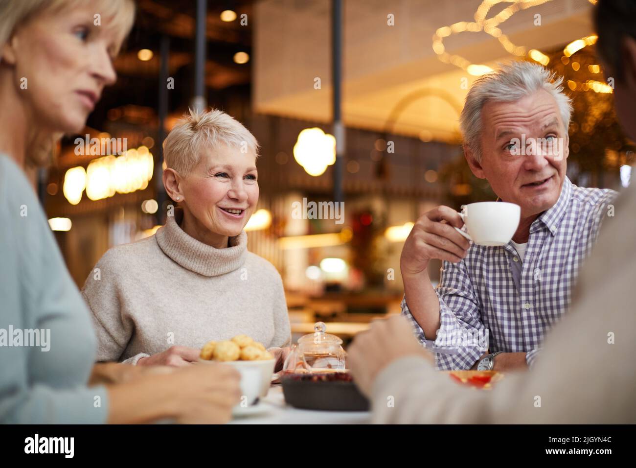 Gruppo di anziani emotivi e positivi seduti a tavola in un moderno caffè e chiacchierando mentre bevono il tè insieme durante il brunch Foto Stock