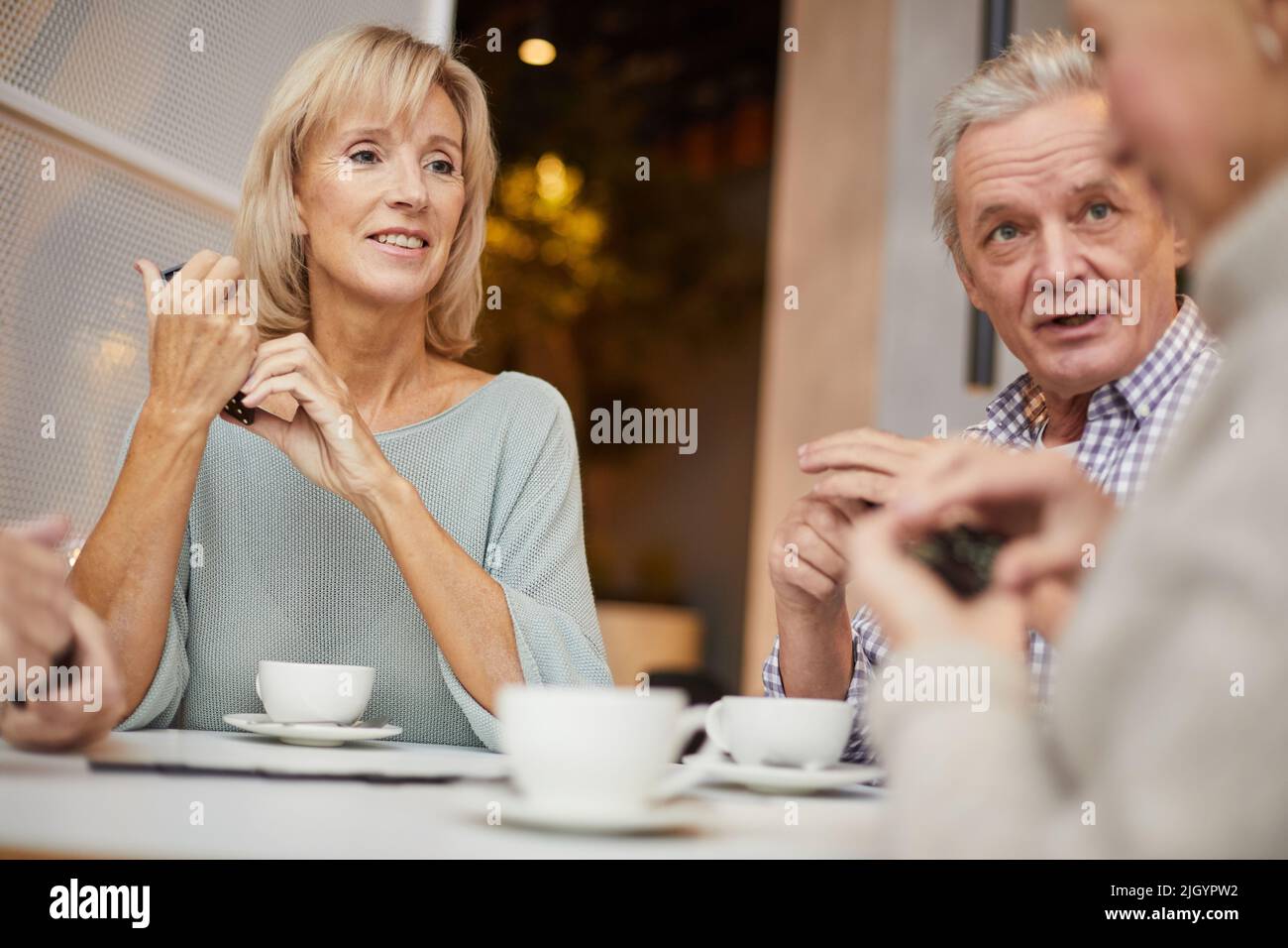 Gruppo di anziani positivi con pezzi di domino in mani seduti a tavola e godendo gioco di domino sopra tazza di tè Foto Stock