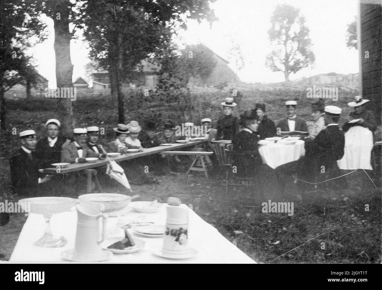 Donne e uomini, probabilmente Harald Falk in berretto studente terzo da destra con il volto alla macchina fotografica, si siede a tavoli lunghi, tavoli con ciotole e caraffe in primo piano. A Grindstugan, Uppsala, intorno al 1900. La foto è inclusa in una raccolta di foto donate da Kerstin Hallström, Uppsala, 8 novembre 1976. Queste immagini sono legate al tempo studentesco di Padre Harald Falk (1895-1905) a Uppsala. Harald Falk visse nella casa studentesca di Norrbyska a Uppsala, appartenne alla nazione Västmanland-Dala, e divenne poi sacerdote a Åtvidaberg, Östergötland e Stora Tuna, Dalarna. Nel 1919 morì in spagnolo Foto Stock