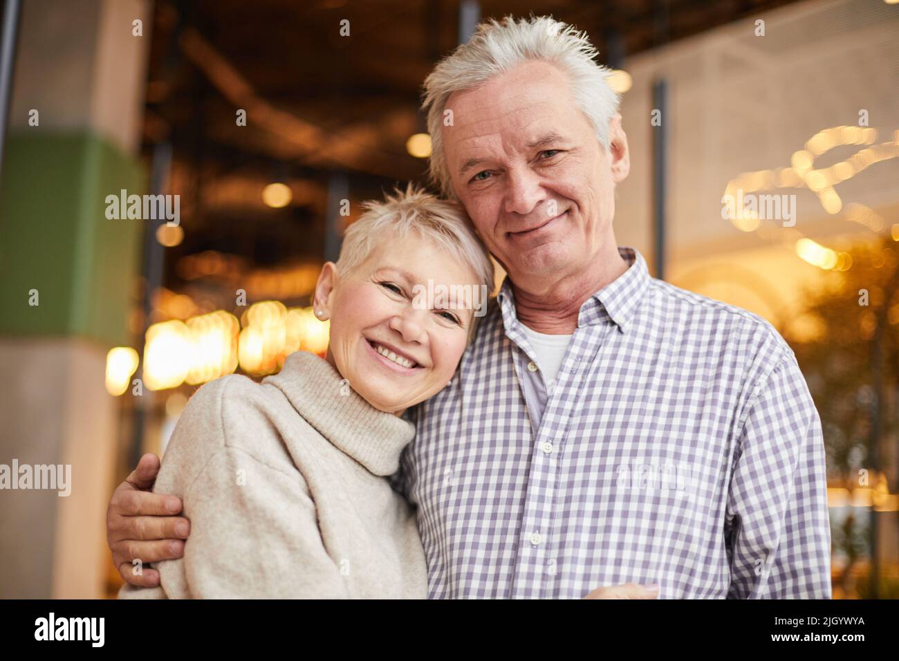 Ritratto di buoni sposi anziani positivi in abiti casual abbracciarsi l'un l'altro in caffè moderno Foto Stock