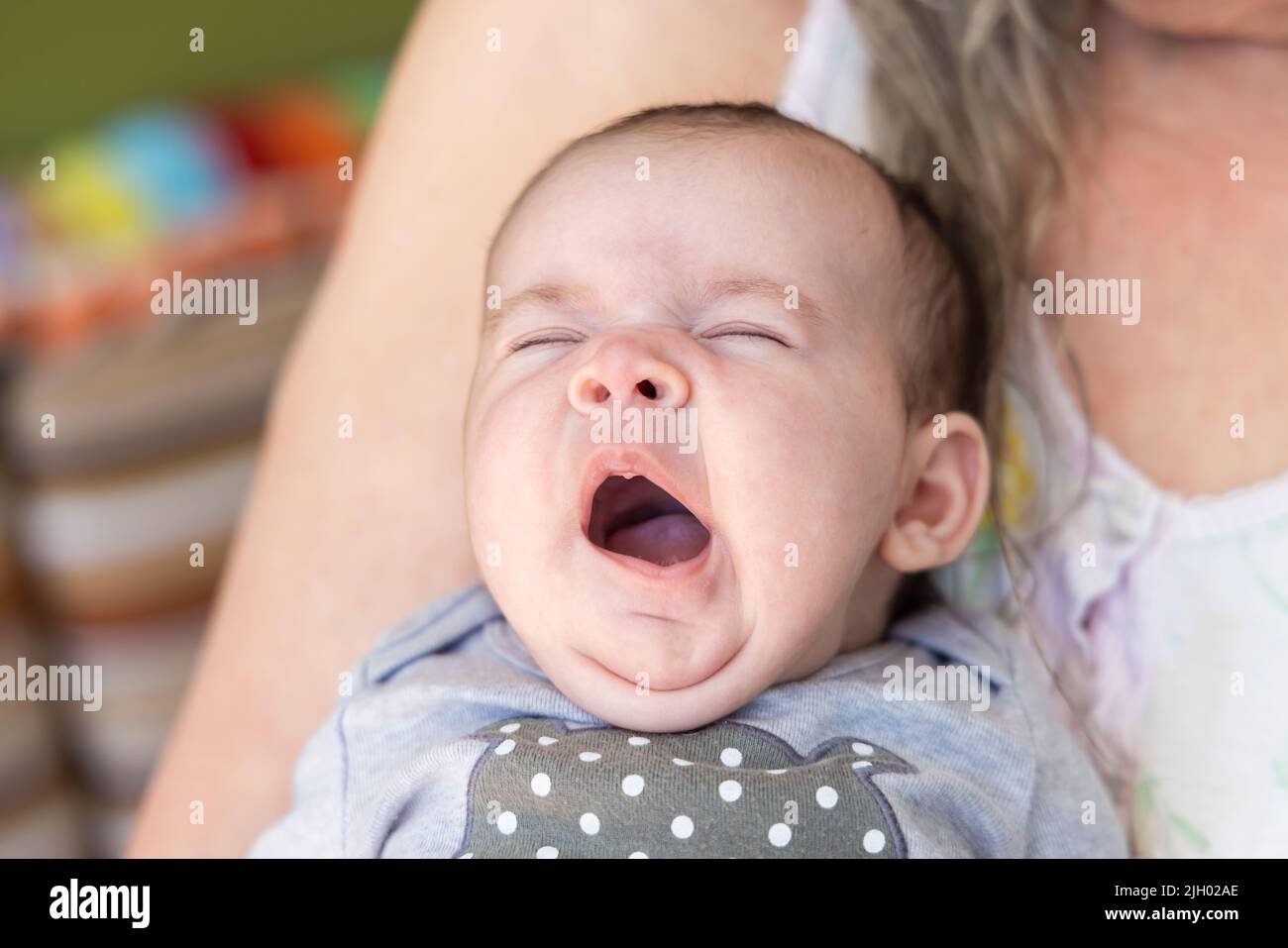 Ritratto heartwarmming di una ragazza del bambino carina di un mese tenuta vicino al petto della nonna. Imbardata del bambino esaurita con gli occhi chiusi. Con spazio di copia. Foto Stock