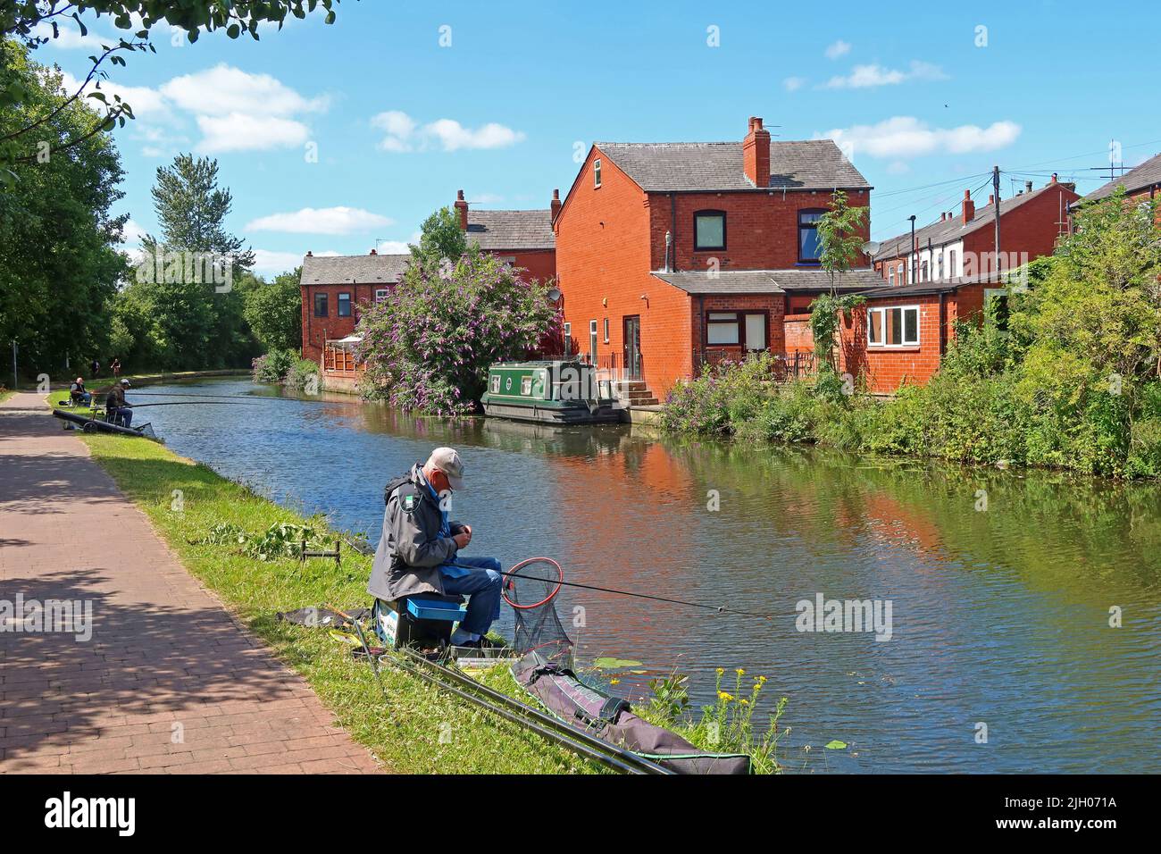 Uomo che pesca con canna & mulinello, sul canale di Bridgewater - ramo di Leigh, Wigan, Lancashire, Inghilterra, Regno Unito, WN7 3AE Foto Stock