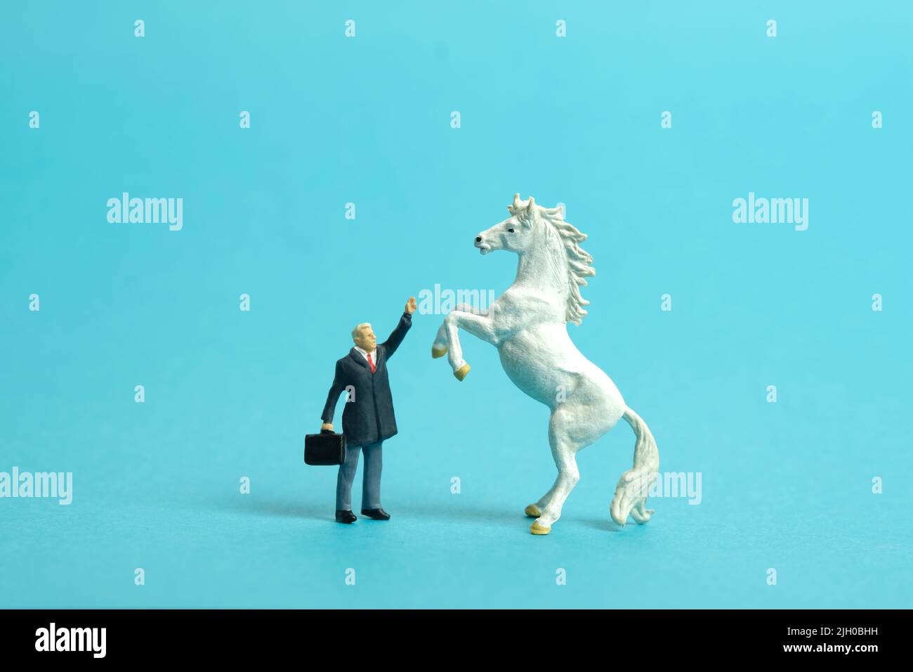 Fotografia di personaggi giocattolo in miniatura. Un uomo d'affari in piedi davanti a cavallo di prancing mentre alza la mano. Isolato su sfondo blu. ph dell'immagine Foto Stock