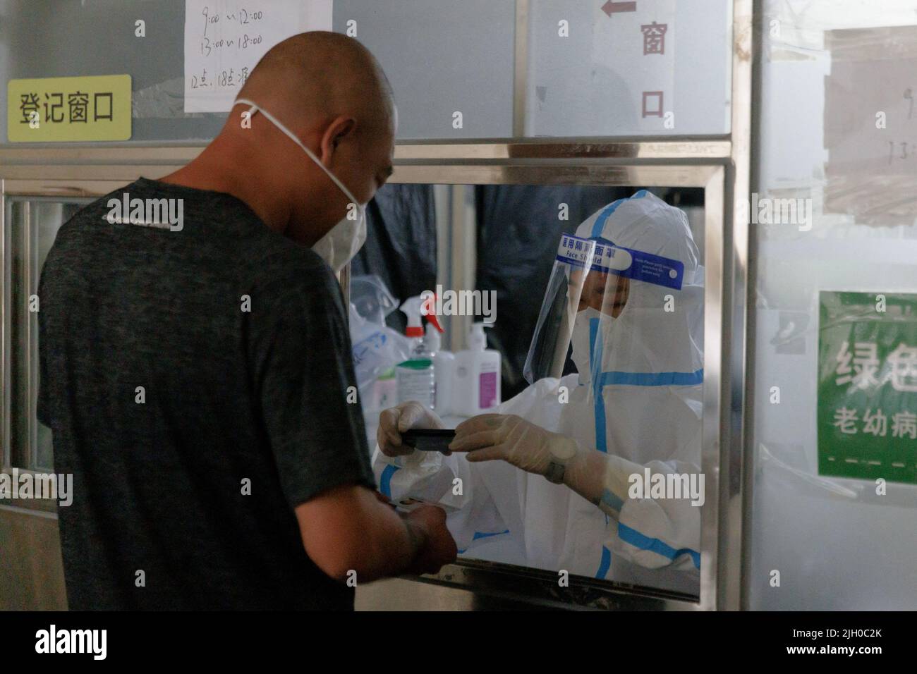 Un operatore medico scansiona la carta d'identità di un uomo in una stazione di analisi degli acidi nucleici, a seguito di un focolaio di coronavirus (COVID-19), a Pechino, Cina, 14 luglio 2022. REUTERS/Thomas Peter Foto Stock