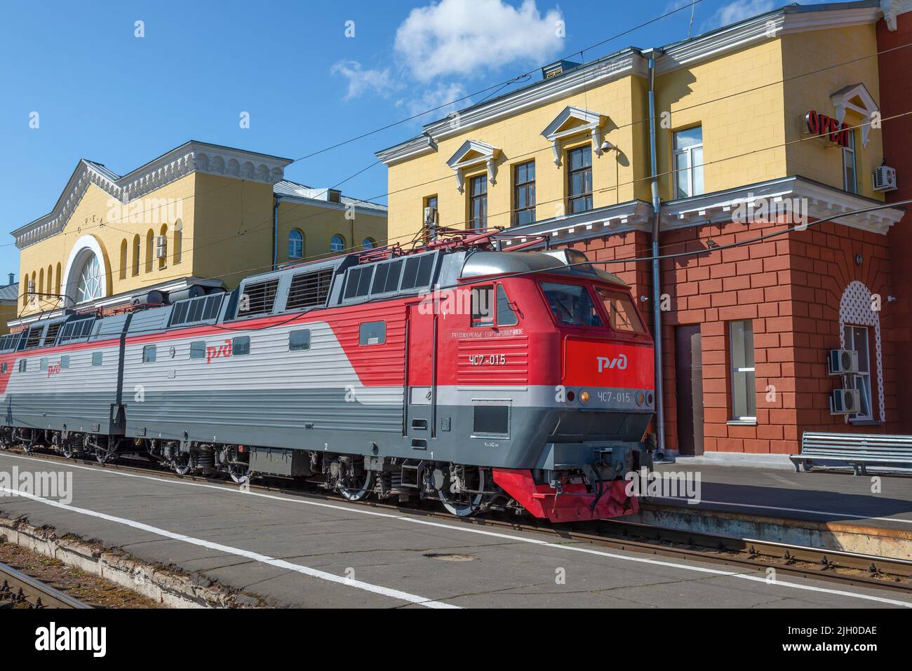 ORYOL, RUSSIA - 06 LUGLIO 2021: Locomotiva elettrica per passeggeri ceca ChS7-015 sullo sfondo dell'edificio della stazione ferroviaria Foto Stock