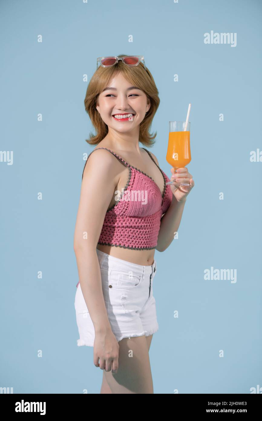 La ragazza asiatica tiene un bicchiere di succo d'arancia tra le braccia e sorride in posa nello studio Foto Stock