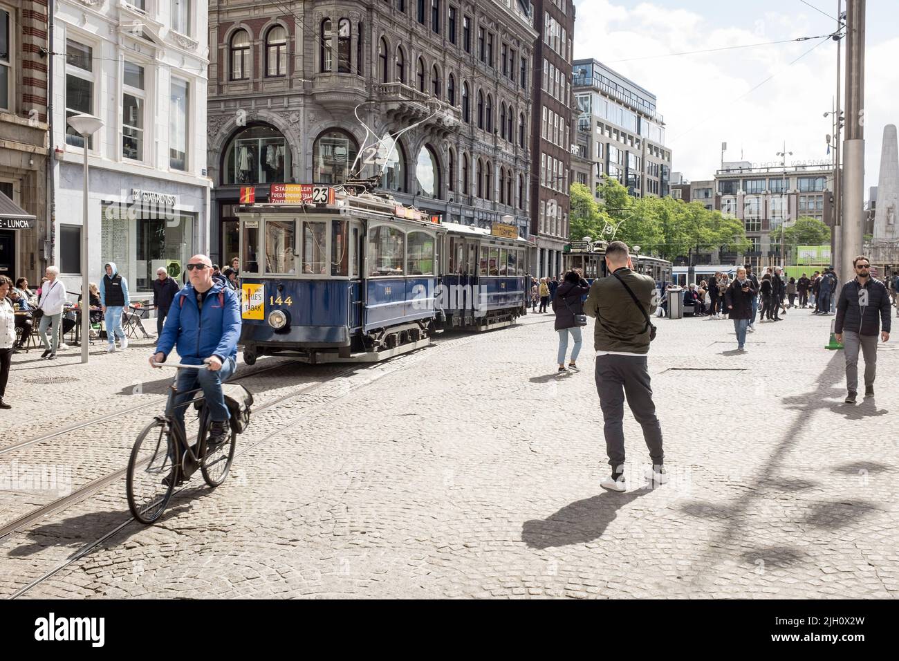 Un uomo passa in bicicletta su un tram d'epoca parcheggiato in una trafficata piazza Dam ad Amsterdam, Paesi Bassi. Foto Stock