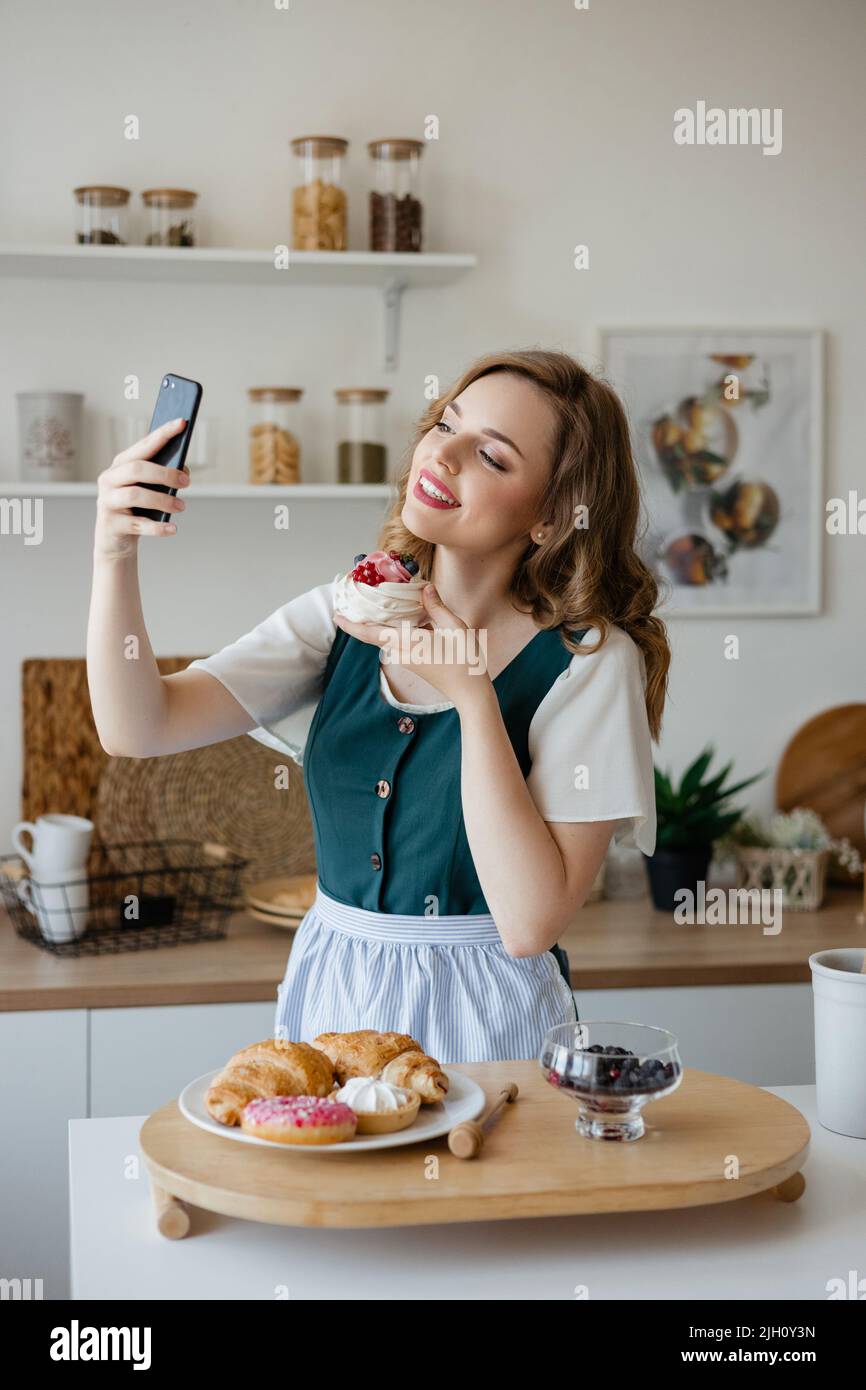 Bella ragazza prende un selfie con una torta in cucina Foto Stock