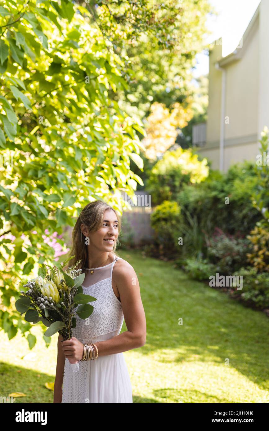 Immagine verticale di felice donna caucasica in abito da sposa che tiene fiori Foto Stock