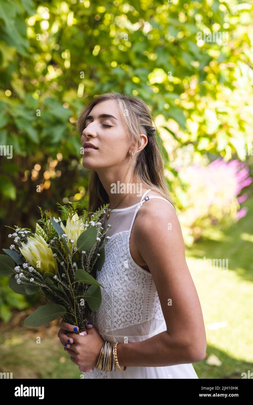 Immagine verticale di felice donna caucasica in abito da sposa che tiene fiori Foto Stock