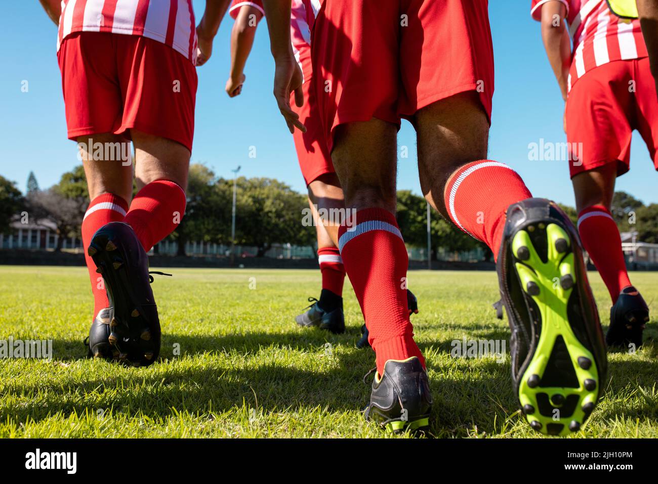 Sezione bassa di atleti maschi multirazziali con uniforme rossa e scarpe da calcio che corrono su terra erbosa Foto Stock