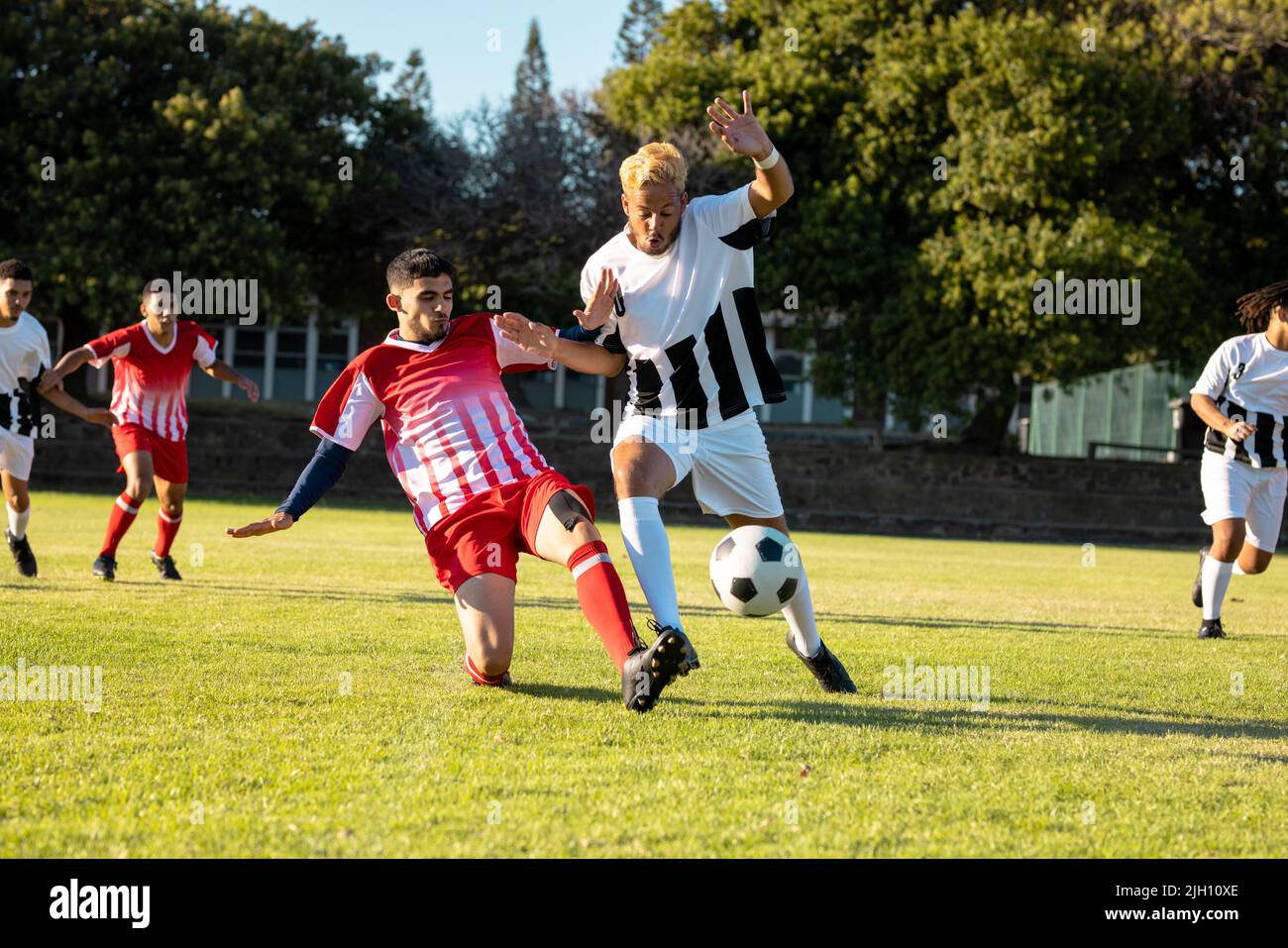 Giocatori multirazziali maschi che corrono e calcia la palla di calcio durante la partita al parco giochi in estate Foto Stock