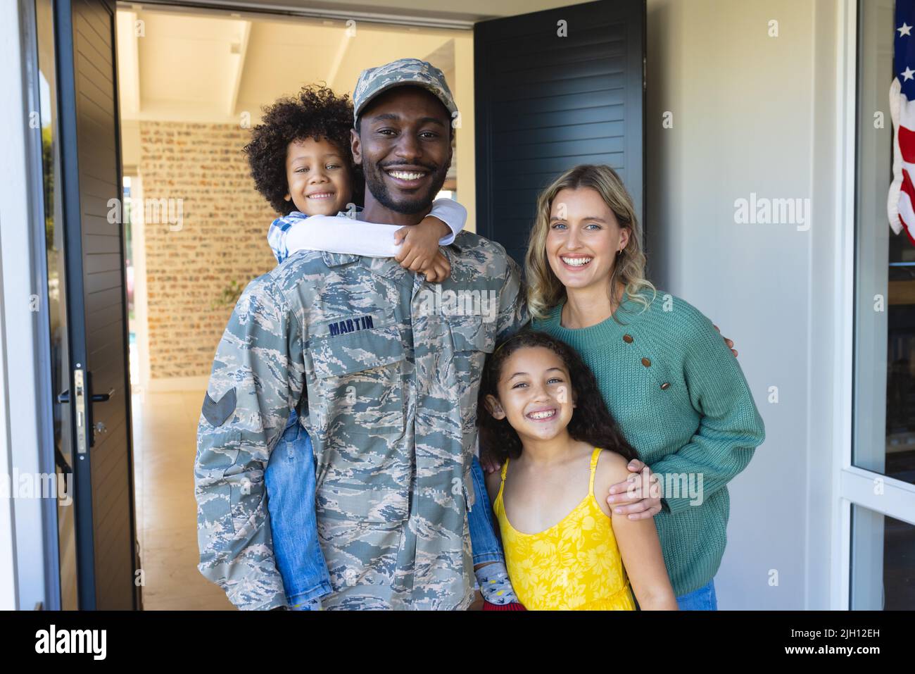 Ritratto di felice soldato multirazziale con donna e bambini in piedi all'ingresso di casa Foto Stock