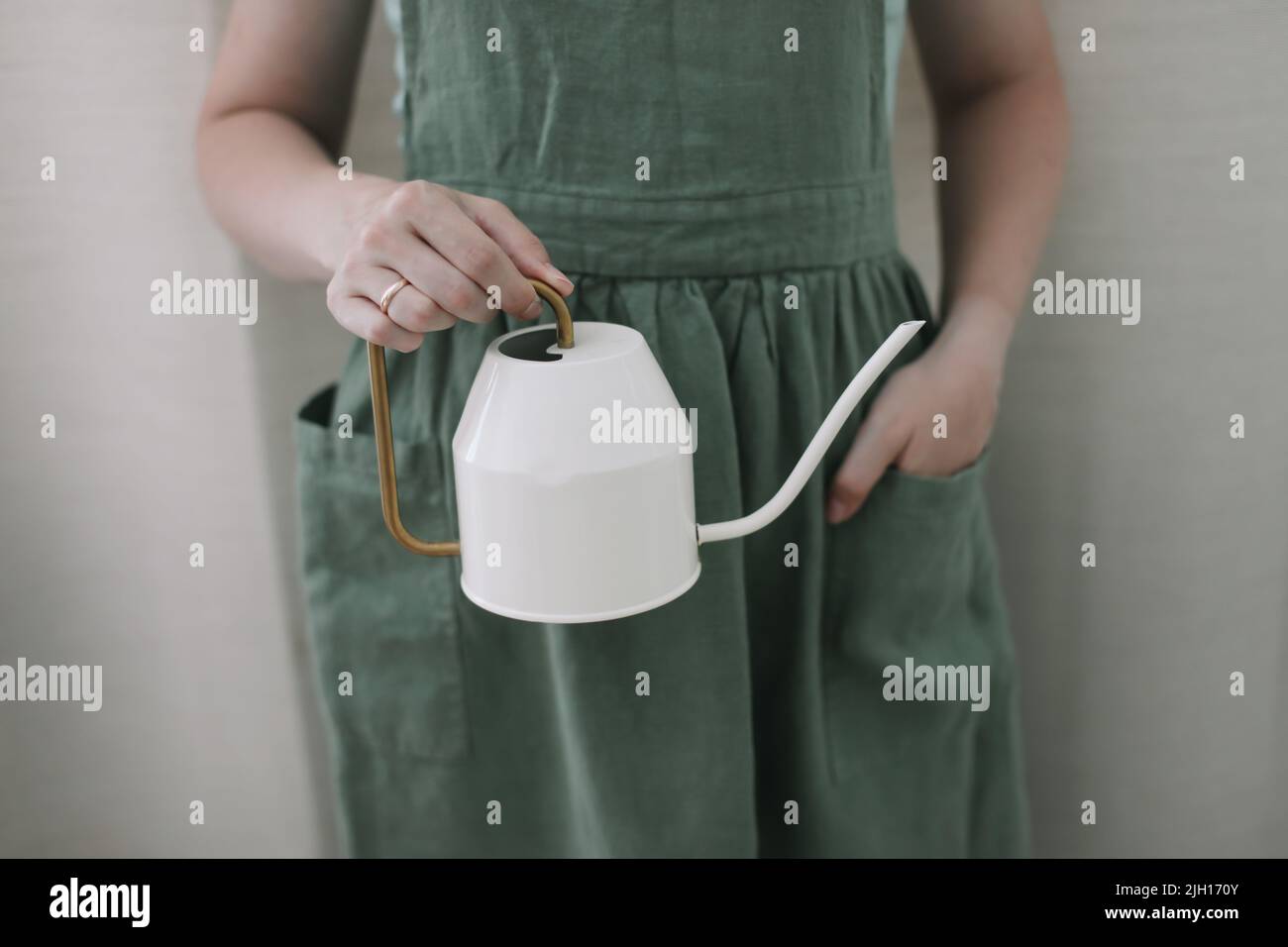 Ragazza in grembiule tiene un annaffiatoio. Annaffiatura e cura di piante domestiche. Giardinaggio domestico. Coltivazione di fiori di hobby Foto Stock