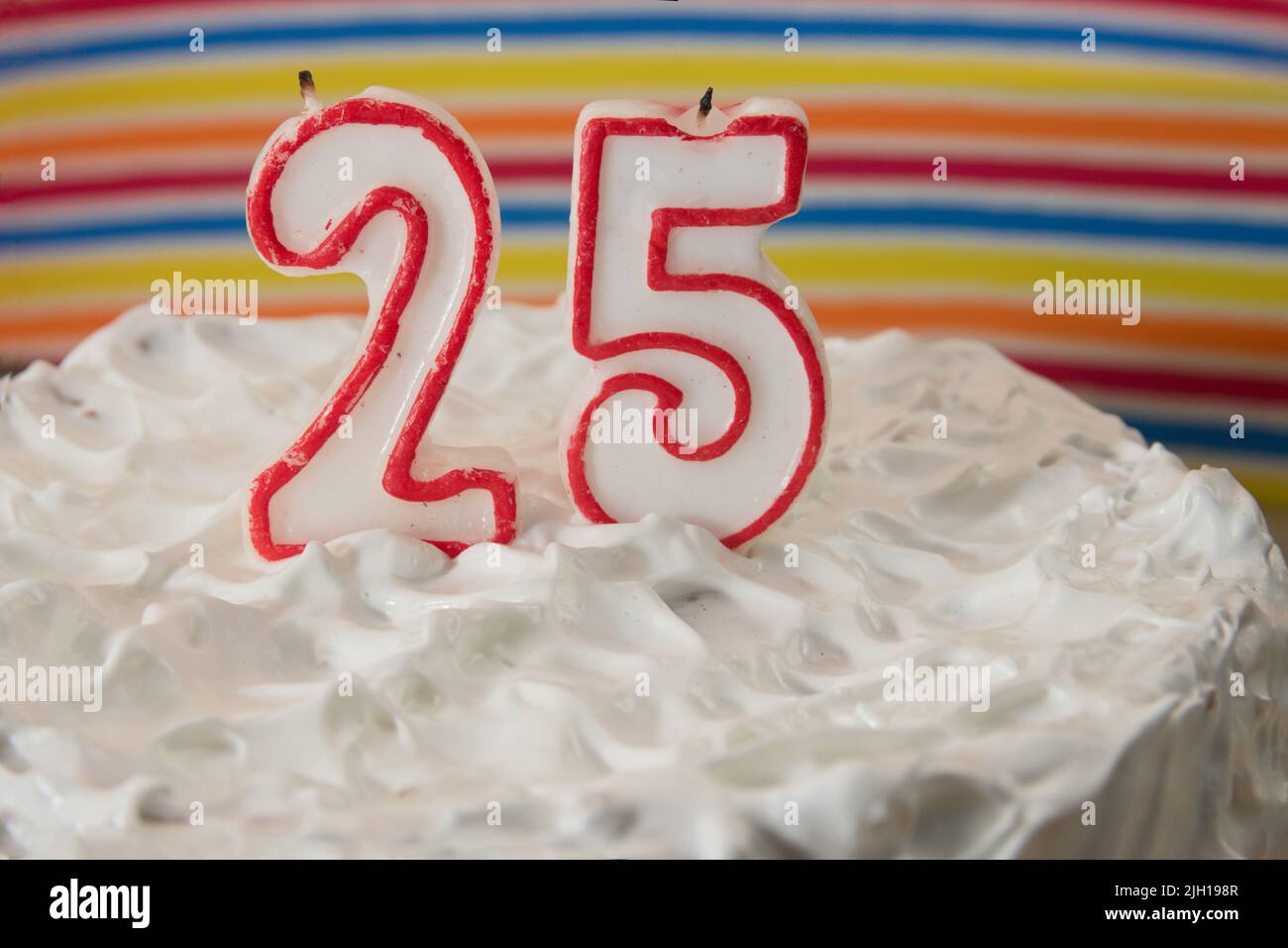 Torta di compleanno o anniversario coperta in meringa fatta in casa con candele a forma di numero 25, sfondo con strisce colorate Foto Stock