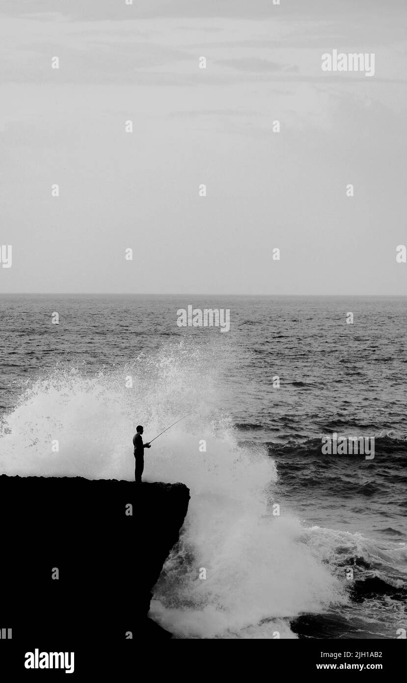 Una silhouette di pescatore in piedi sul bordo sullo sfondo delle onde di mare che infrangono la scogliera Foto Stock Una silhouette di pescatore in piedi sul bordo sullo sfondo delle onde di mare che infrangono la scogliera Foto Stock