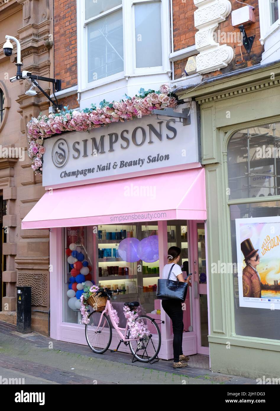 Lincoln, Lincolnshire, Regno Unito, giugno 16 2022 Una giovane donna entra in un salone di bellezza dipinto di rosa con una bicicletta floreale corrispondente parcheggiata all'esterno. Foto Stock