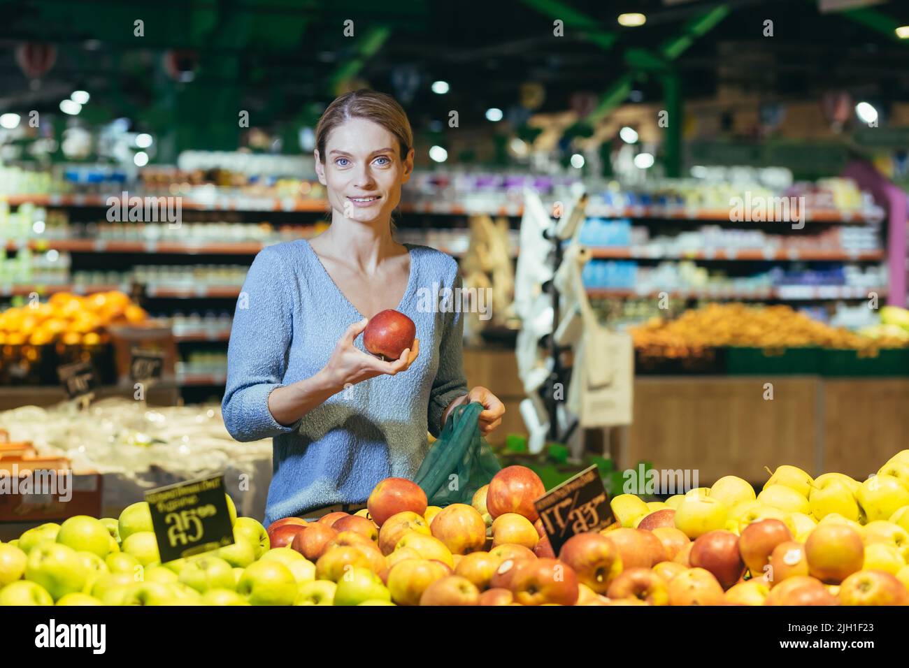 la donna sceglie frutta verdura sul banco in supermercato. Donna casalinga shopping nel mercato in piedi vicino magazzino di verdure con un cestino in mani. Esamina Apple Foto Stock