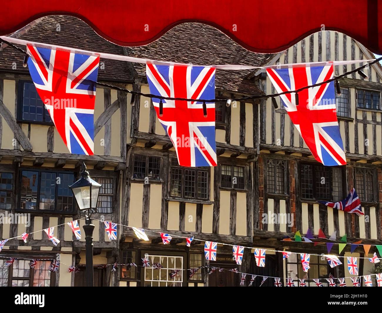 Thaxted Essex England Union Jack Flags and old Buildings Luglio 2022 Union Jack bandiere flutter di fronte a Dick Turpins House e il 14th secolo Guildhall Foto Stock