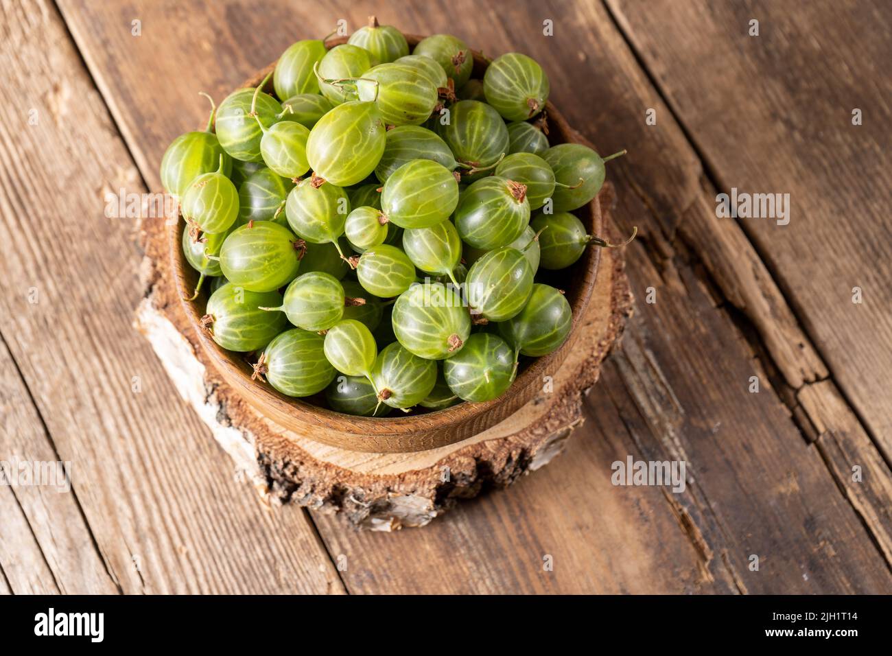 Frutti di bosco verdi in una ciotola di legno. Raccogliere bacche su un tavolo di legno. Cibo vitaminico estivo di uva spina. Foto Stock