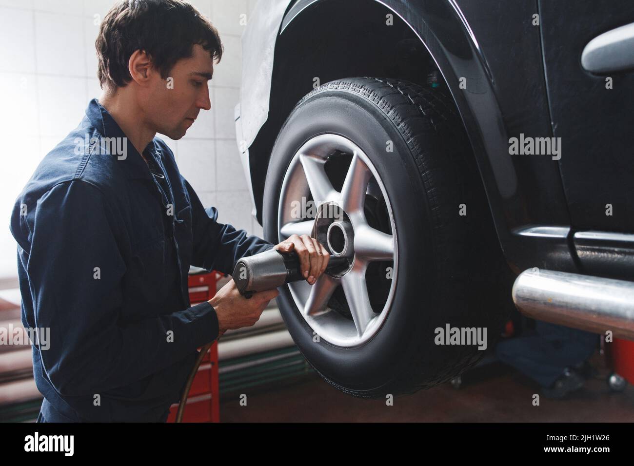 Meccanico che cambia la ruota dell'automobile in officina di riparazione auto Foto Stock