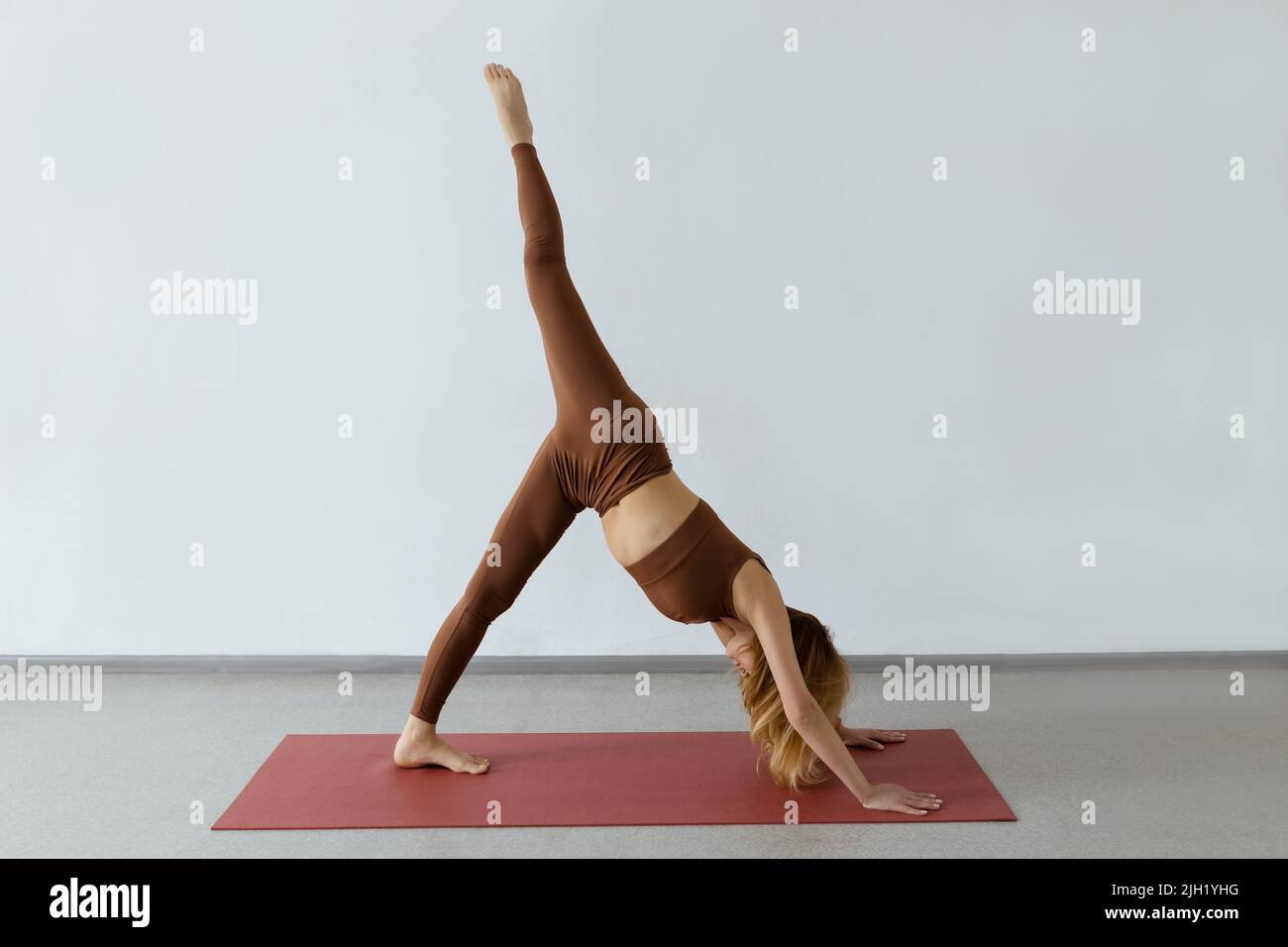 Giovane donna snella che pratica verso il basso cane asana con gamba sollevata, Ekapada Adhomukha Shvanasana Foto Stock