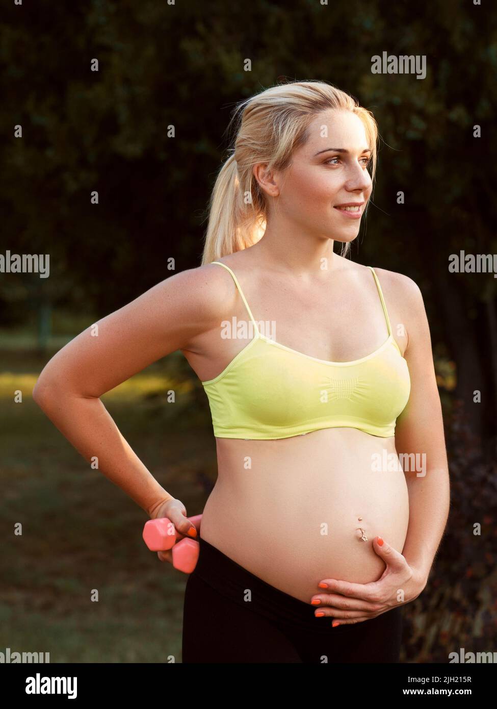Donna incinta sorridente carezzerà il ventre alla natura Foto Stock