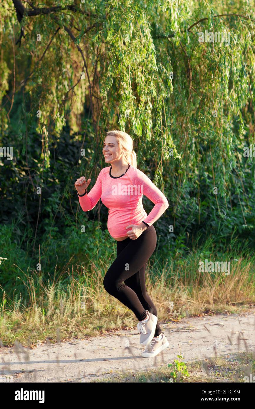 Donna incinta felice che fa jogging fuori Foto Stock