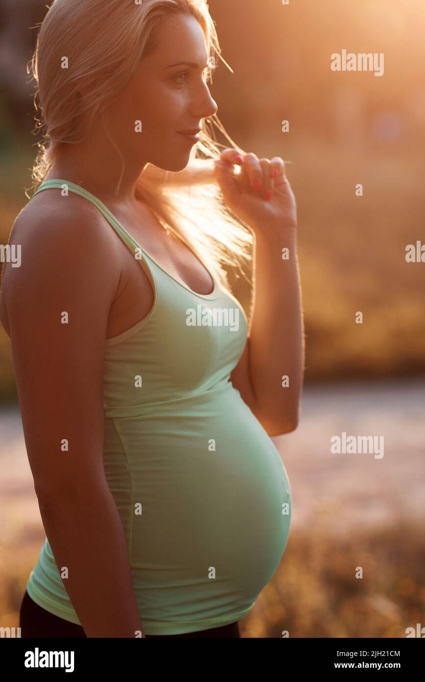 Profilo di bionda incinta con aspetto pensivo Foto Stock