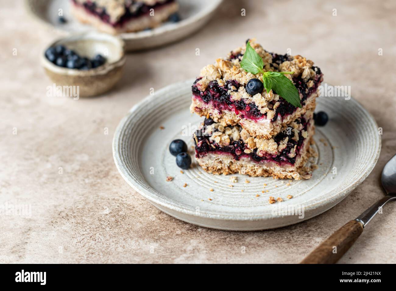 Barre di mirtillo crumble fatte in casa su un piatto decorato con menta su sfondo beige. Composizione sana della colazione, spazio di testo. Orientamento orisontale Foto Stock