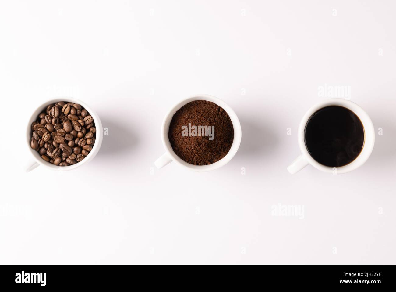 Immagine di tre tazze piene di caffè macinato, chicchi di caffè e caffè su sfondo bianco Foto Stock