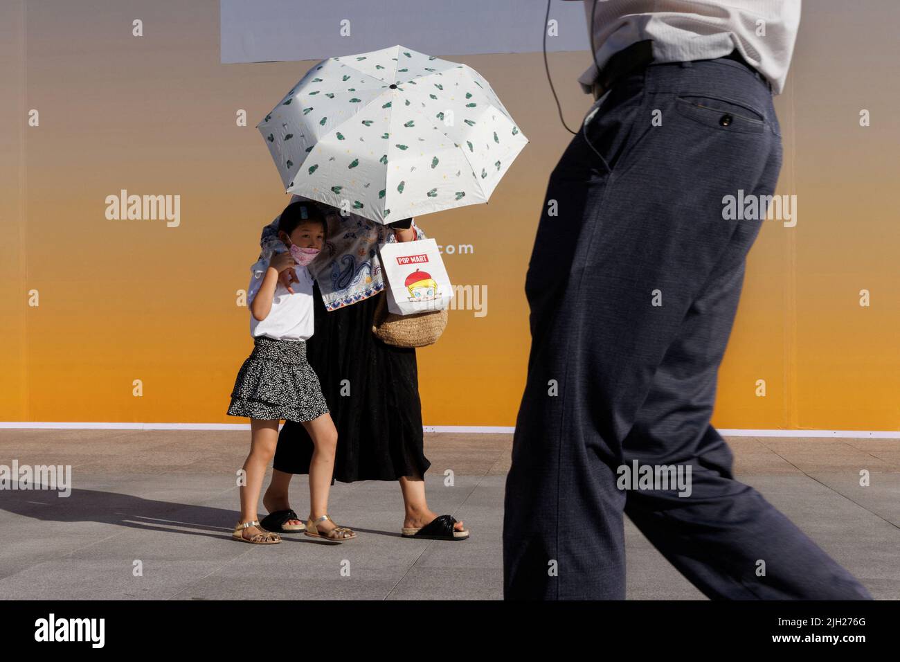 Una donna e un bambino cercano una copertura dal sole sotto un ombrellone in una zona commerciale a Pechino, Cina, 14 luglio 2022. REUTERS/Thomas Peter Foto Stock