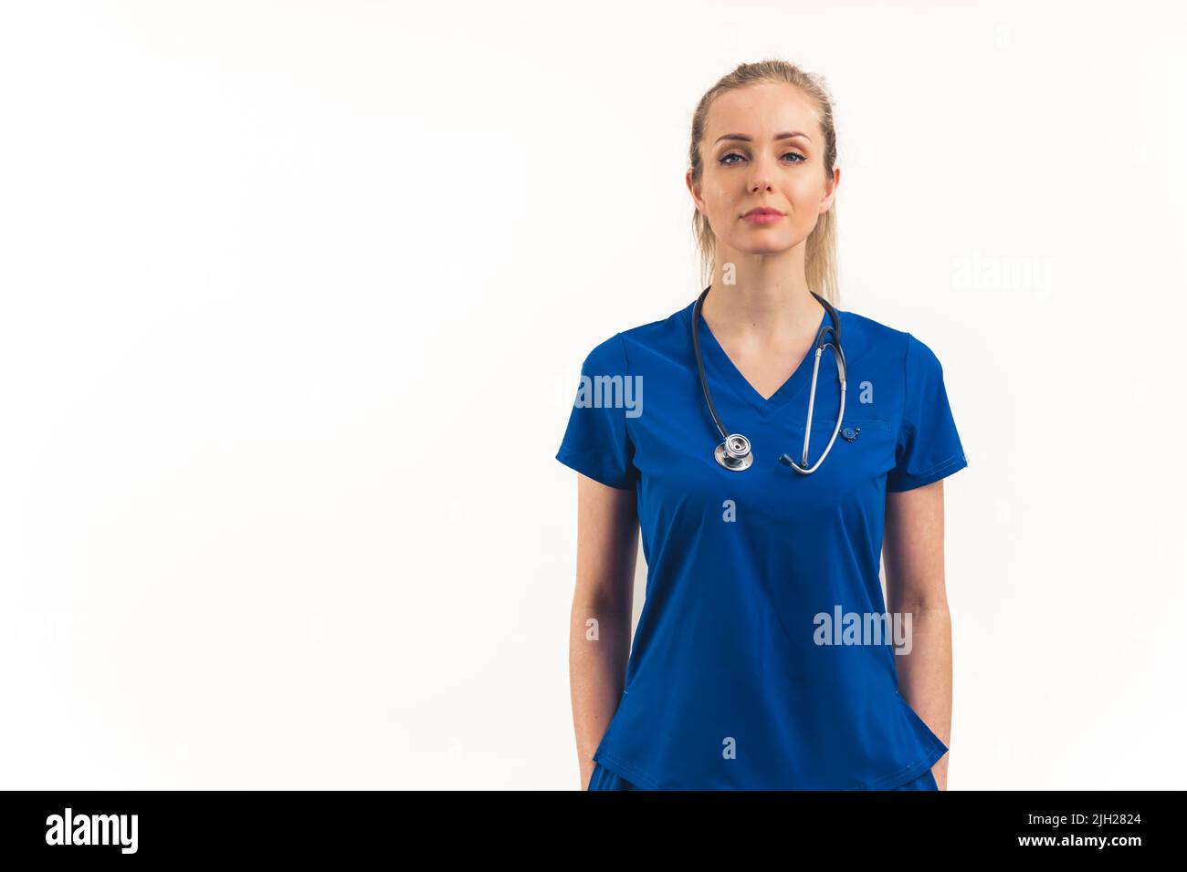 Specialisti sanitari come eroi moderni. Medico professionista europeo biondo giovane adulto in uniforme blu scuro e stetoscopio guardando con sicurezza alla macchina fotografica. Studio medio girato su sfondo bianco. Spazio di copia isolato. Foto di alta qualità Foto Stock