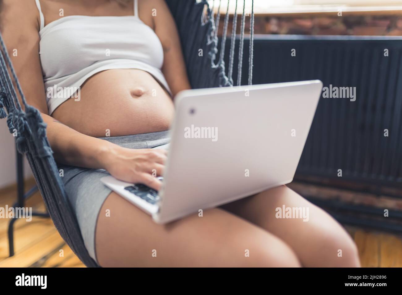 Primo piano di una ventre incinta e di un notebook argento. Informazioni sul parto e sul lavoro online. Attività per il tempo libero. Foto di alta qualità Foto Stock