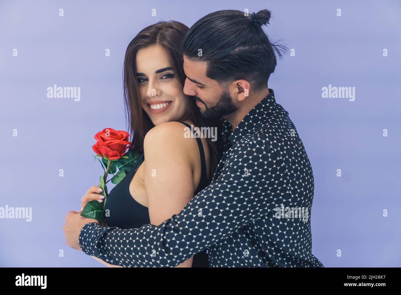 Fiore sorpresa. Bell'uomo cubano bearded dai capelli scuri che abbraccia la sua amata giovane moglie dalla schiena e le dà una bella rosa rossa. . Foto di alta qualità Foto Stock